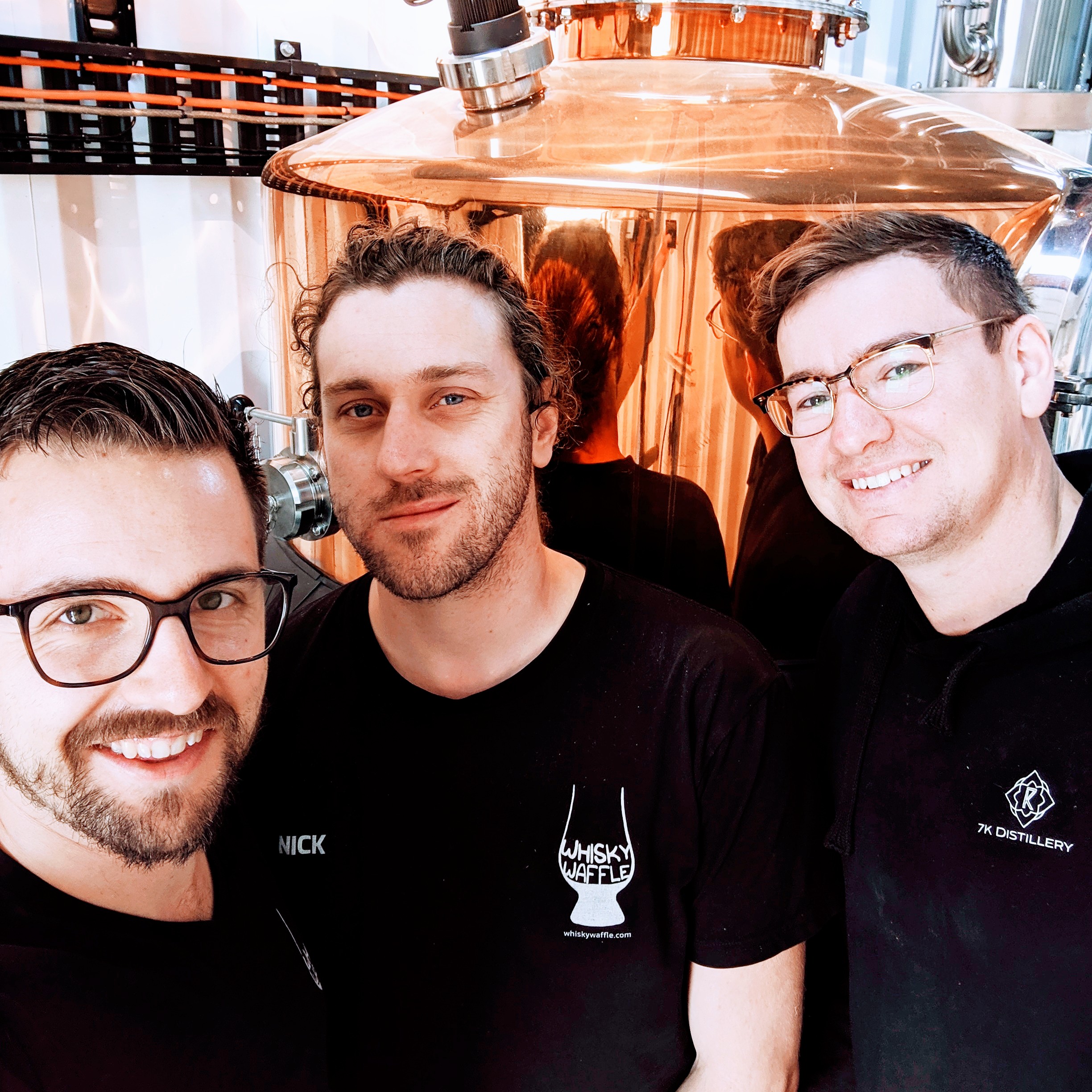 Three men standing in front of a whisky still. Two of them are Nick and Ted, world famous whisky writers from the blog Whisky Waffle. The other man is Tyler Clark, the owner of 7K Distillery